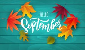 Teal wooden background with the words Hello September, surrounded by colorful fall leaves.